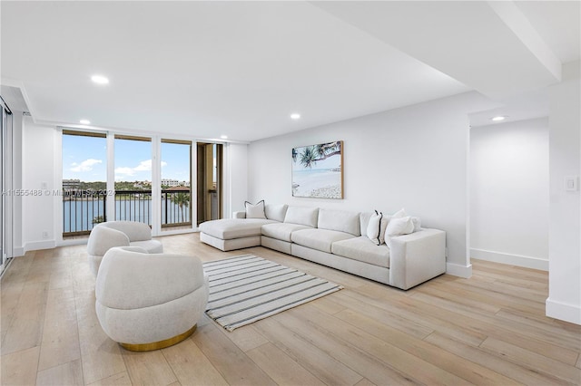 living room featuring light hardwood / wood-style flooring, floor to ceiling windows, and a water view