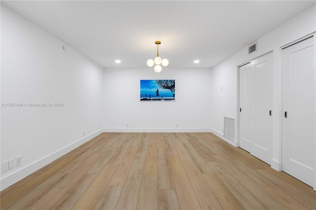 unfurnished room featuring an inviting chandelier and light hardwood / wood-style flooring