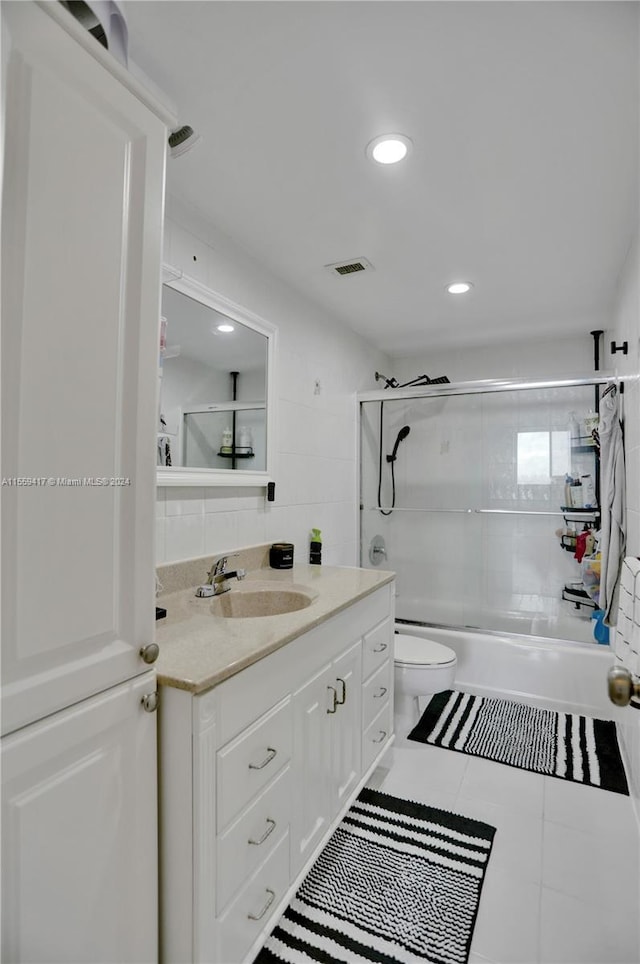 full bathroom featuring toilet, tile walls, vanity, tiled shower / bath combo, and tile patterned flooring