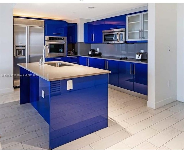 kitchen featuring sink, an island with sink, light tile floors, blue cabinetry, and stainless steel appliances