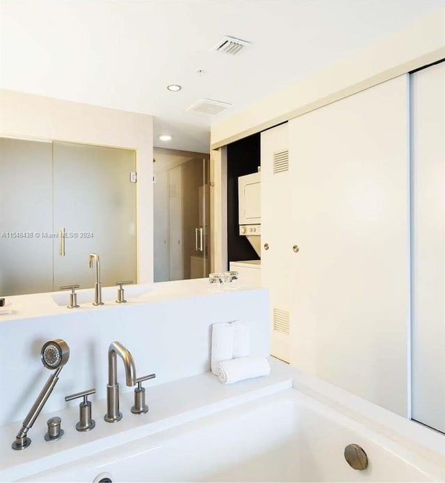 bathroom with dual sinks, vanity with extensive cabinet space, and stacked washer / drying machine