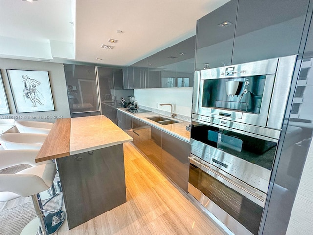 kitchen featuring black electric cooktop, stainless steel double oven, sink, a center island, and light wood-type flooring