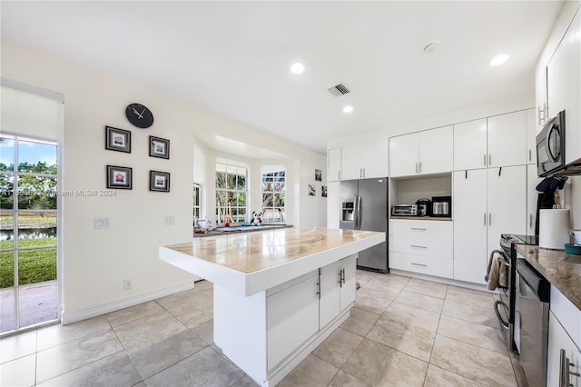 kitchen with light tile floors, appliances with stainless steel finishes, a kitchen bar, white cabinetry, and a center island