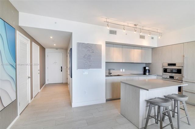 kitchen with double oven, a breakfast bar, track lighting, sink, and a center island