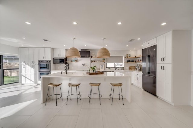 kitchen featuring appliances with stainless steel finishes, white cabinets, an island with sink, and a wealth of natural light