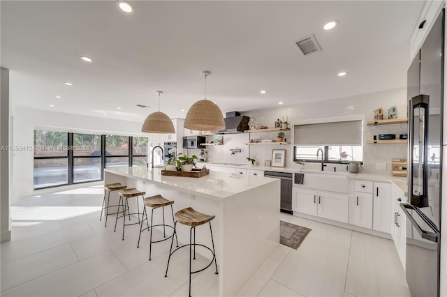 kitchen featuring white cabinetry, a center island with sink, stainless steel appliances, pendant lighting, and light tile floors