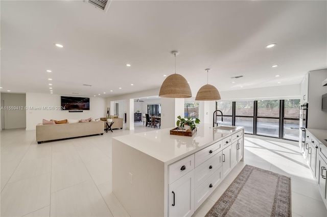 kitchen with light tile floors, white cabinetry, hanging light fixtures, and a center island with sink