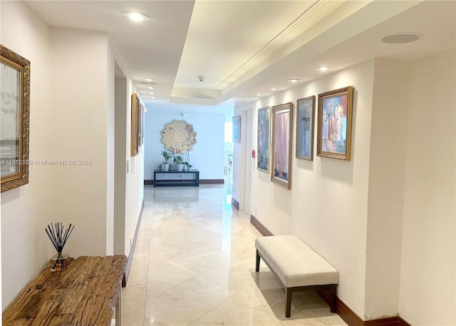 hallway featuring light tile flooring and a tray ceiling