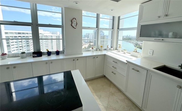 kitchen with cooktop, light tile floors, white cabinetry, and sink