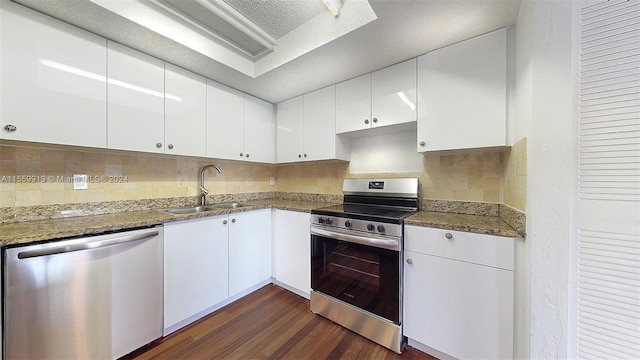 kitchen with white cabinetry, dark hardwood / wood-style floors, dark stone countertops, stainless steel appliances, and backsplash