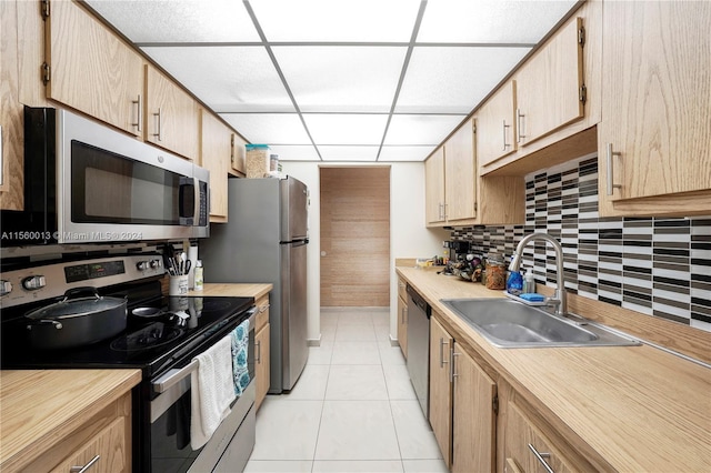 kitchen featuring light tile flooring, backsplash, stainless steel appliances, sink, and a paneled ceiling