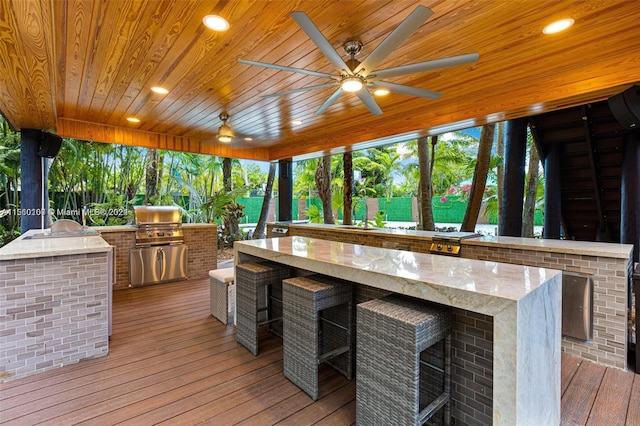 wooden terrace with exterior kitchen, exterior bar, ceiling fan, and grilling area