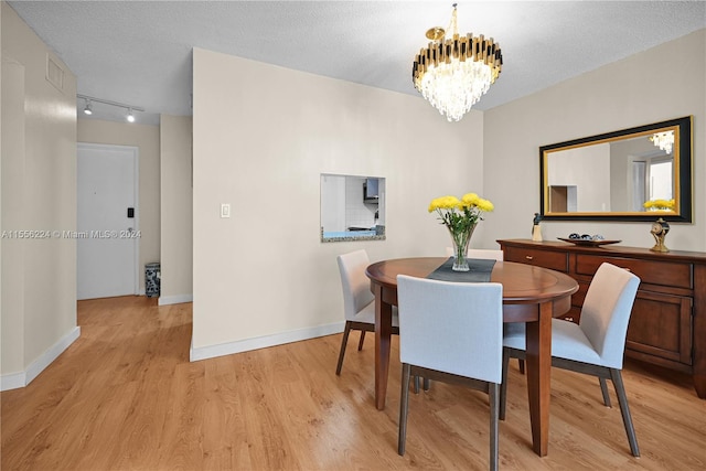 dining room with rail lighting, a textured ceiling, a notable chandelier, and light hardwood / wood-style floors