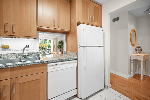 kitchen with white appliances, light tile patterned floors, backsplash, light stone countertops, and sink