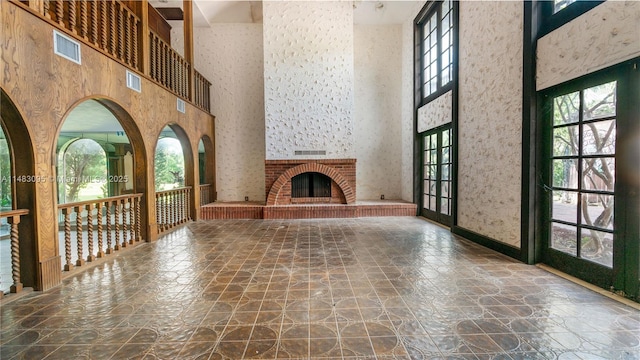 unfurnished living room with visible vents, stone finish floor, a brick fireplace, and a towering ceiling