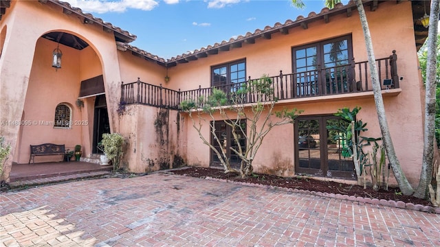 back of house featuring a balcony, a patio area, stucco siding, and french doors