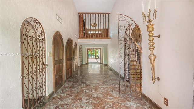 hall featuring visible vents, arched walkways, baseboards, marble finish floor, and a high ceiling