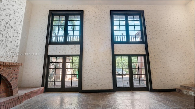 doorway featuring a high ceiling, a fireplace, stone tile flooring, and baseboards