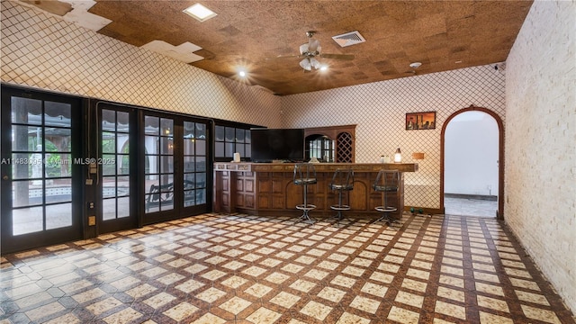 interior space with arched walkways, ceiling fan, visible vents, a community bar, and wallpapered walls