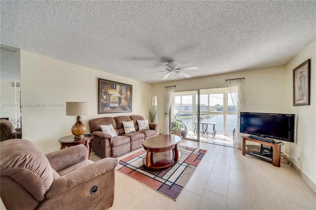 tiled living room with a water view, a textured ceiling, and ceiling fan