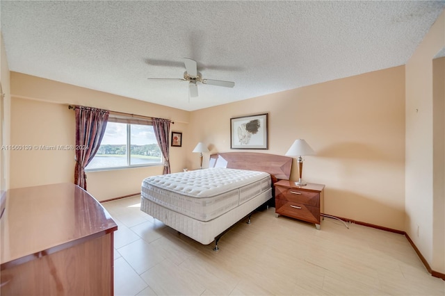 bedroom featuring a water view, a textured ceiling, ceiling fan, and light tile floors