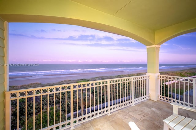 balcony at dusk featuring a water view and a beach view