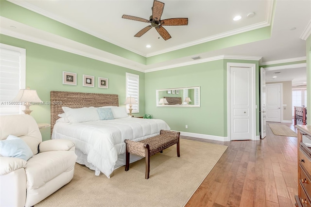 bedroom featuring light wood-type flooring, ornamental molding, a tray ceiling, and ceiling fan