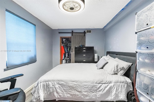 bedroom featuring a barn door, visible vents, wood finished floors, a spacious closet, and a closet