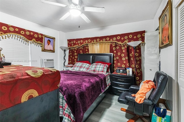 bedroom featuring a wall unit AC, ceiling fan, and wood finished floors