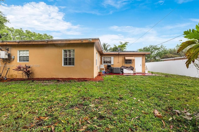 back of house with a yard, fence, and stucco siding