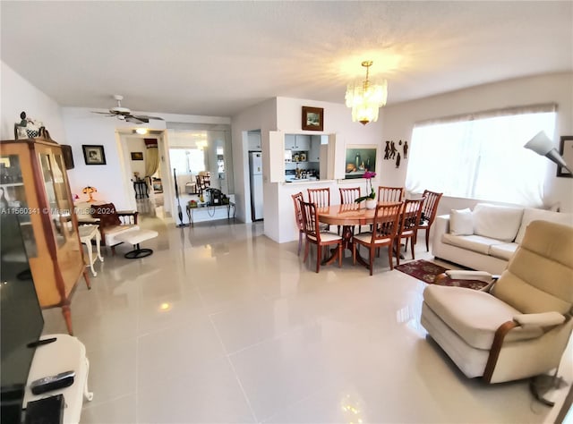 tiled living room with ceiling fan with notable chandelier