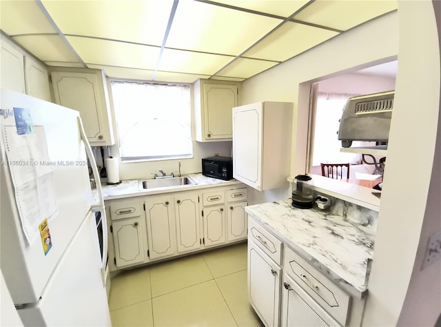 kitchen featuring cream cabinets, light tile floors, white refrigerator, and sink