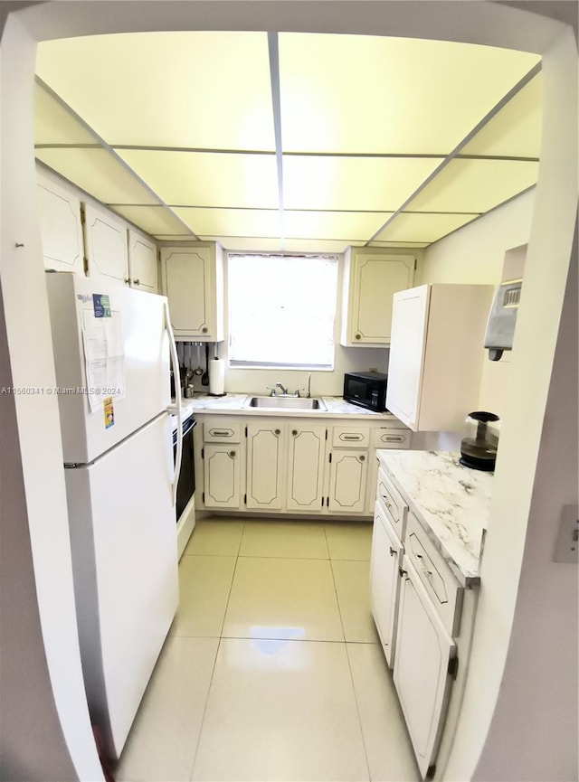 kitchen with sink, light tile floors, stove, white refrigerator, and cream cabinetry