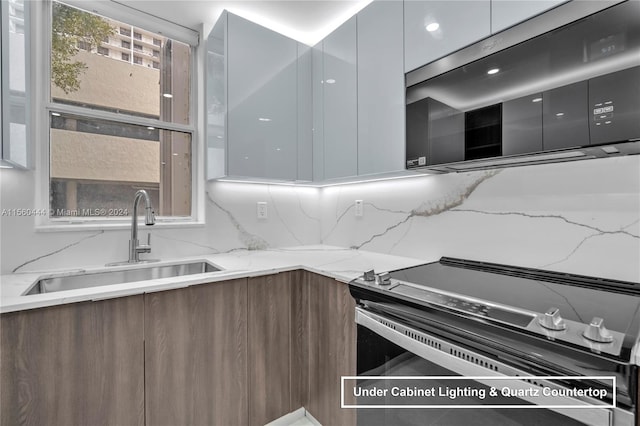 kitchen featuring backsplash, electric range, sink, and light stone countertops