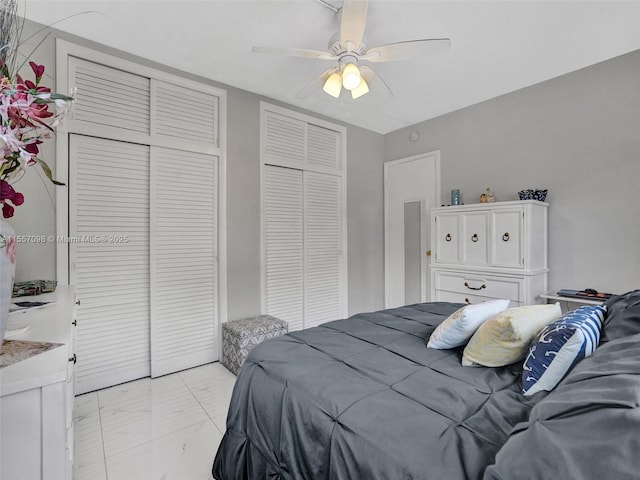 bedroom with marble finish floor, ceiling fan, and two closets