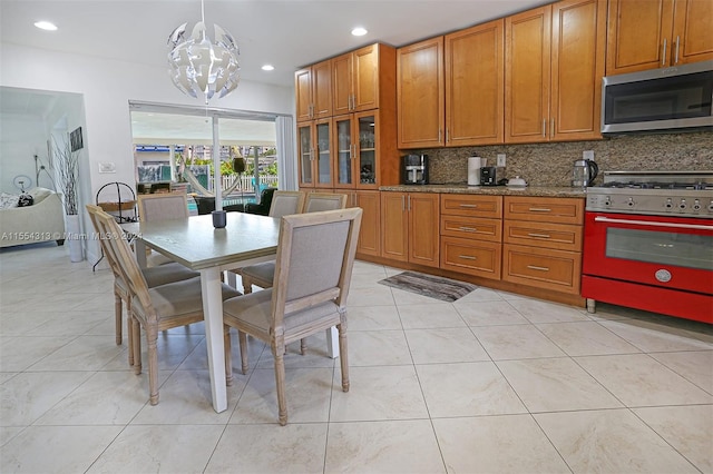 kitchen with tasteful backsplash, light stone counters, range, light tile patterned floors, and pendant lighting