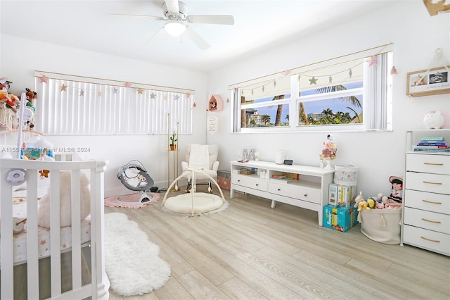 bedroom featuring a nursery area, ceiling fan, and light hardwood / wood-style flooring