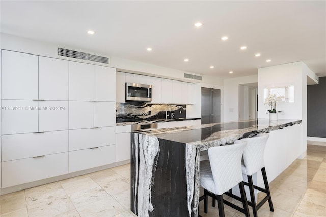 kitchen with white cabinets, dark stone counters, a kitchen breakfast bar, and stainless steel appliances