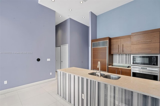 kitchen featuring a high ceiling, black microwave, light tile flooring, sink, and stainless steel oven