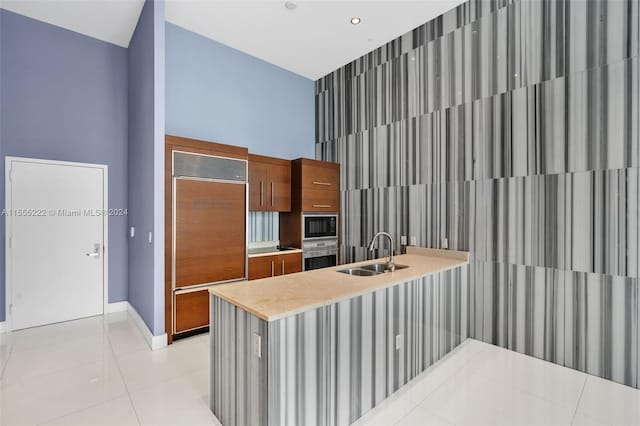 kitchen featuring built in appliances, light tile flooring, sink, and kitchen peninsula