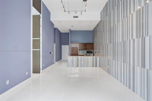 hall featuring sink, light tile floors, a towering ceiling, and track lighting