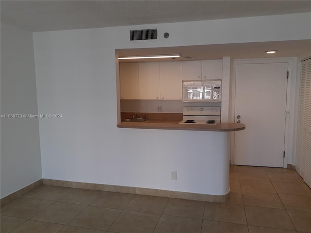 kitchen with white cabinets, built in microwave, range, and light tile flooring