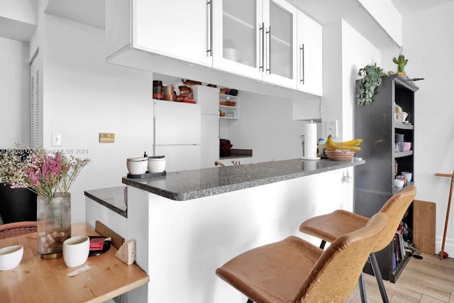 kitchen with white cabinets, white refrigerator, light hardwood / wood-style flooring, kitchen peninsula, and a breakfast bar area