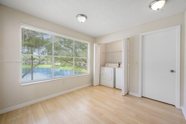 unfurnished bedroom featuring washer and dryer, light hardwood / wood-style floors, multiple windows, and a textured ceiling