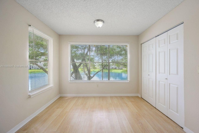 unfurnished bedroom featuring light hardwood / wood-style floors, a textured ceiling, and multiple windows