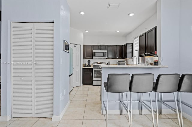 kitchen featuring light tile floors, kitchen peninsula, dark brown cabinetry, and stainless steel appliances