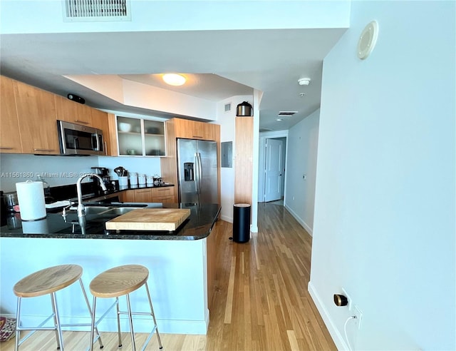 kitchen with appliances with stainless steel finishes, kitchen peninsula, a breakfast bar area, and light hardwood / wood-style flooring