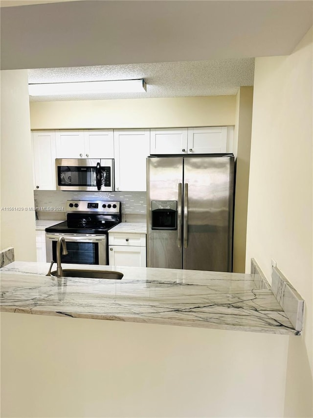 kitchen featuring tasteful backsplash, light stone countertops, white cabinets, and appliances with stainless steel finishes