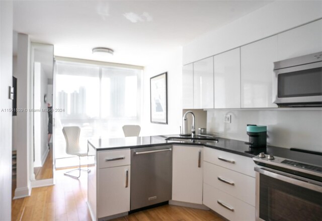 kitchen featuring white cabinets, sink, appliances with stainless steel finishes, light hardwood / wood-style flooring, and kitchen peninsula