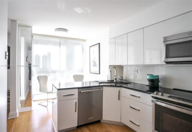 19101 Mystic Pointe Dr Unit 1411, Aventura, FL 33180 - kitchen with appliances with stainless steel finishes, white cabinets, sink, light hardwood / wood-style flooring, and kitchen peninsula